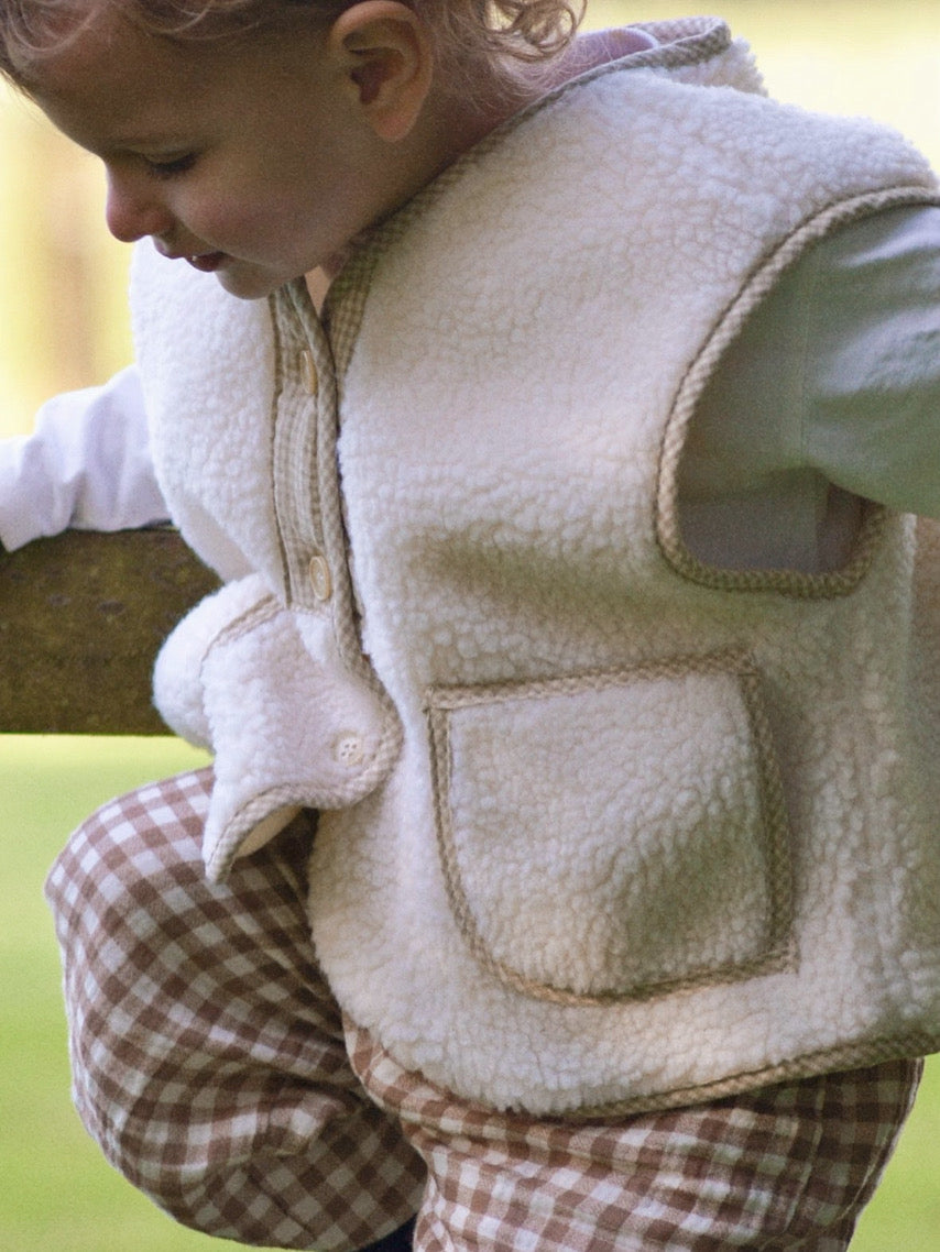 Child wearing a cream boucle gilet stood on fence with a blurred background