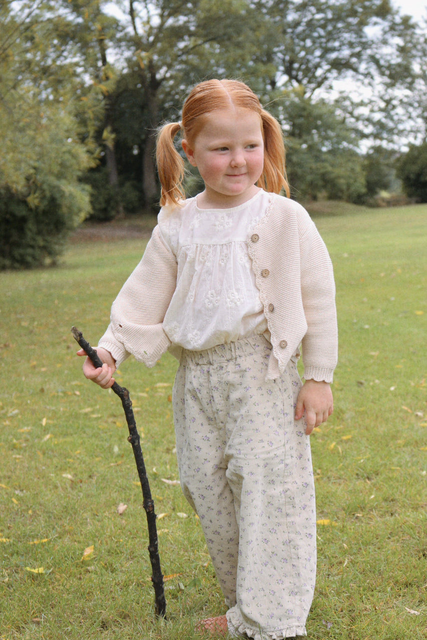 Young girl in vintage inspired clothing holding a walking stick in a park.