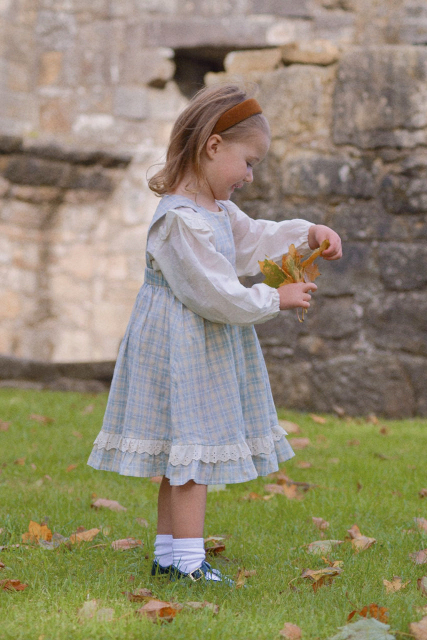 Young girl in a light dress holding a leaf in front of a stone wall.