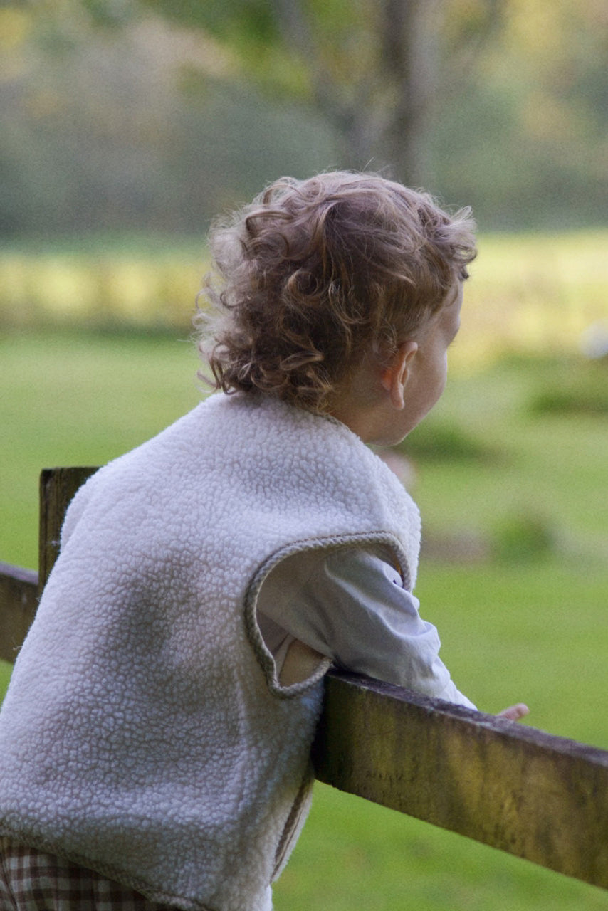 Child sitting on a wooden bench looking out over a green field