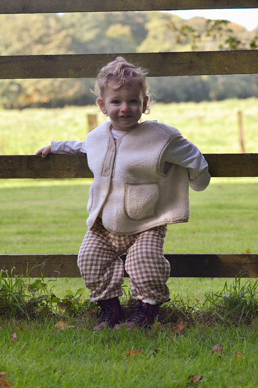 Child wearing a cream boucle gilet stood against fence with a blurred background