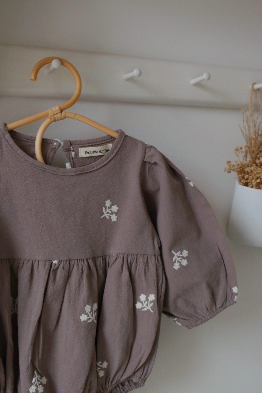 Grey Romper with floral embroidery on a wooden hanger against a neutral wall.