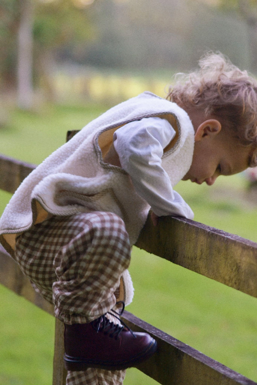 Child wearing a cream boucle gilet stood on fence with a blurred background