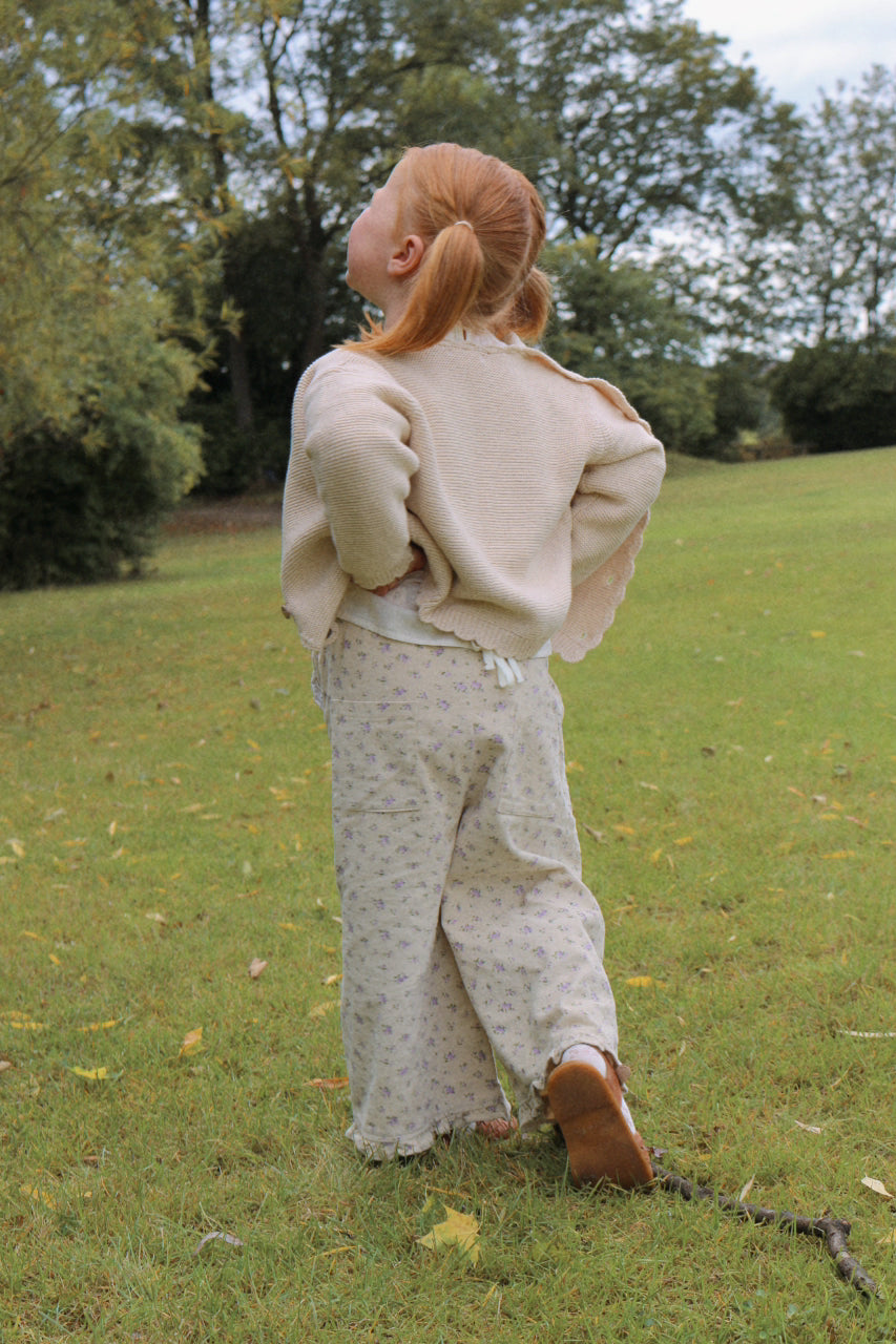 Girl wearing a beige outfit standing in a grassy field with trees in the background