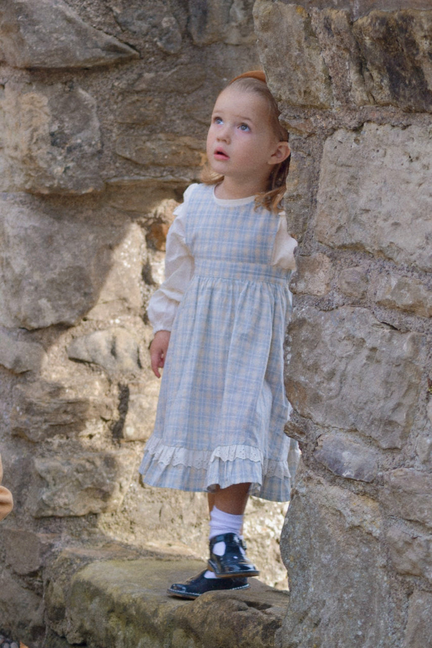 Young girl in a checkered dress standing against a stone wall