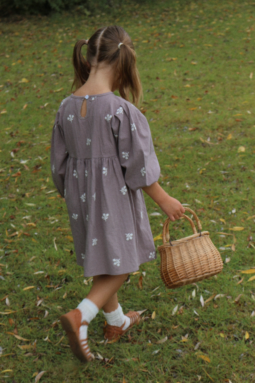 Child in a purple dress holding a wicker basket on a grassy field