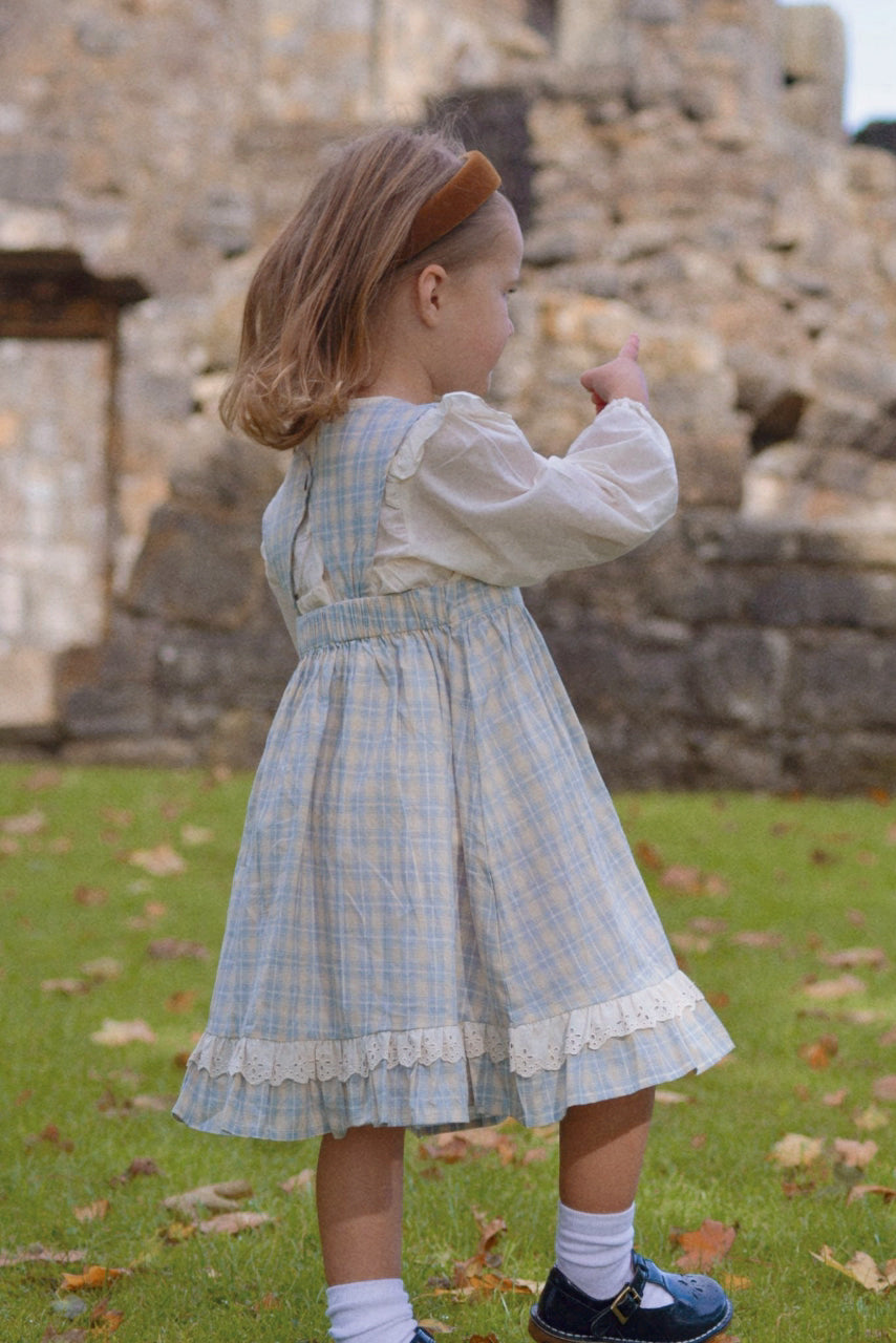 Young girl in a blue checkered dress standing in front of stone ruins.