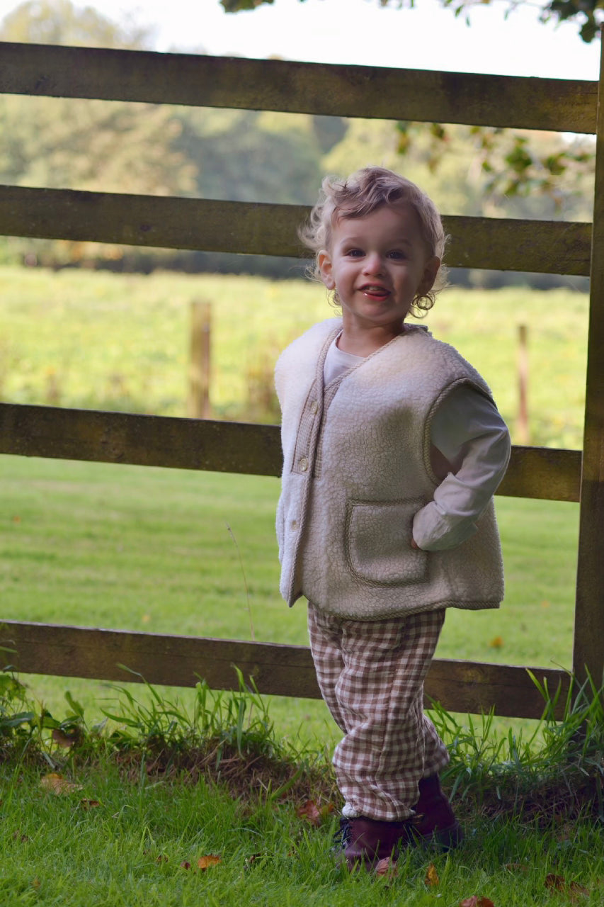Child standing in a grassy field with a wooden fence in the background