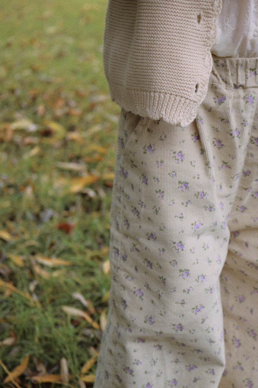 Girl wearing a beige cardigan and floral pants standing on grass