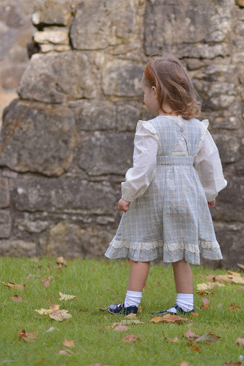 Child in a checkered dress standing in front of a stone wall