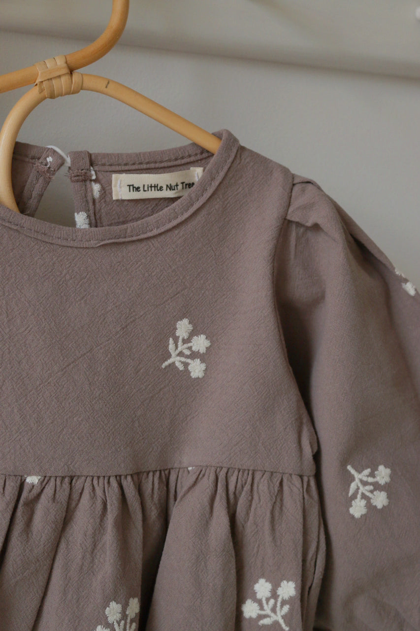 Grey romper with ivory floral patterns on a hanger against a neutral background