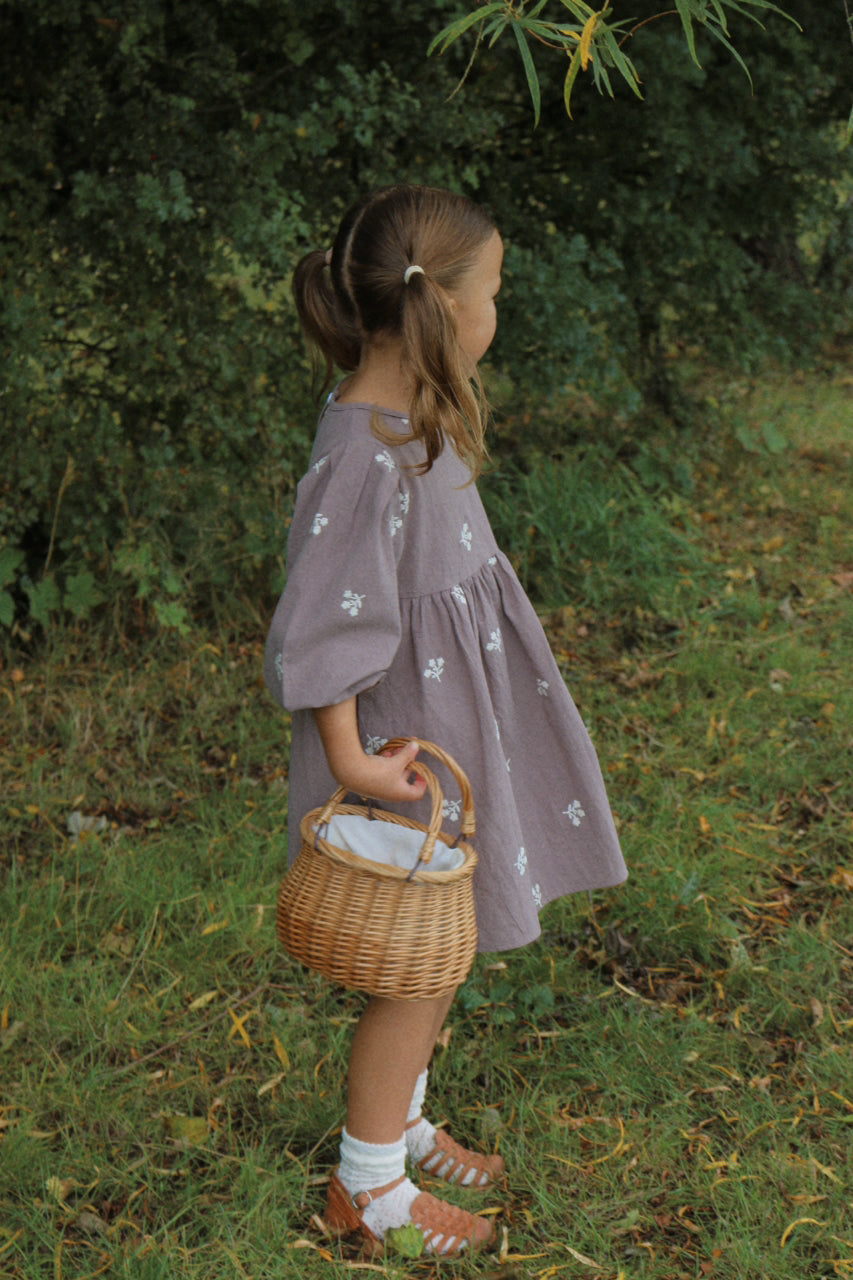 Young girl in a grey dress holding a wicker basket in a natural setting.