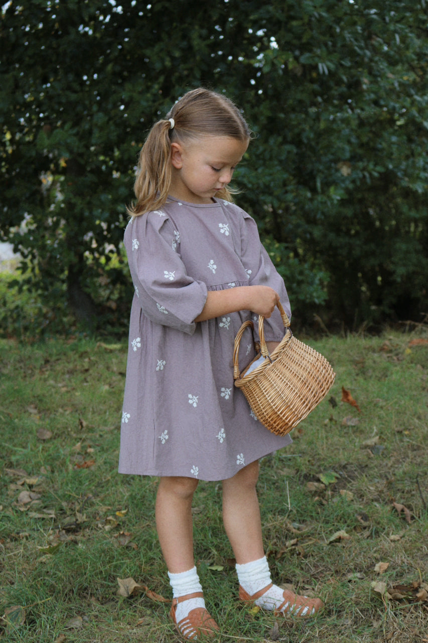 Young girl in a purple dress holding a wicker basket outdoors.