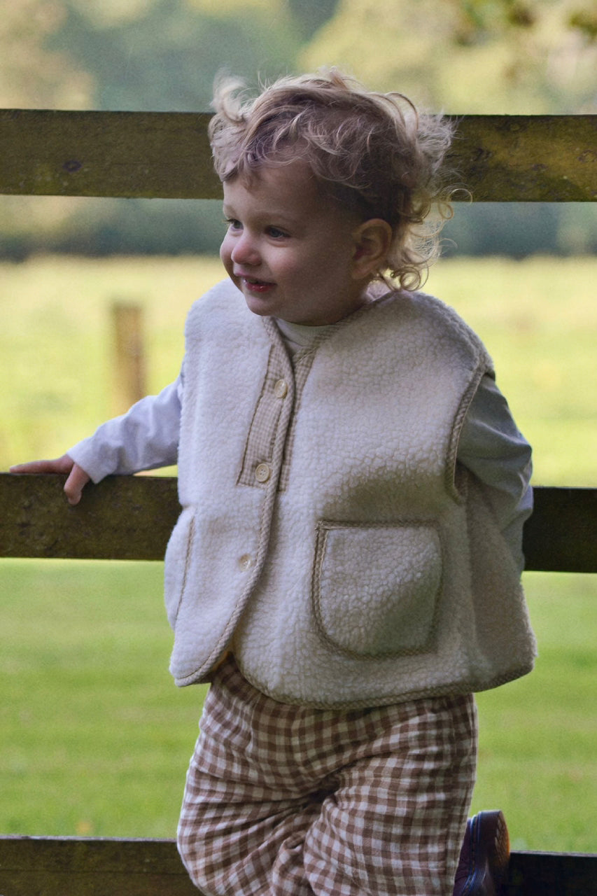 Child wearing a cream boucle gilet stood on fence with a blurred background