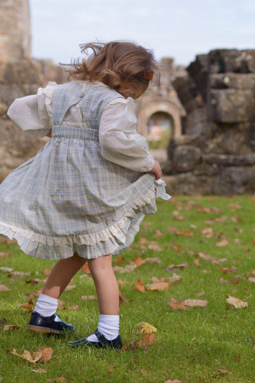 Child in a checkered dress standing on grass with ruins in the background