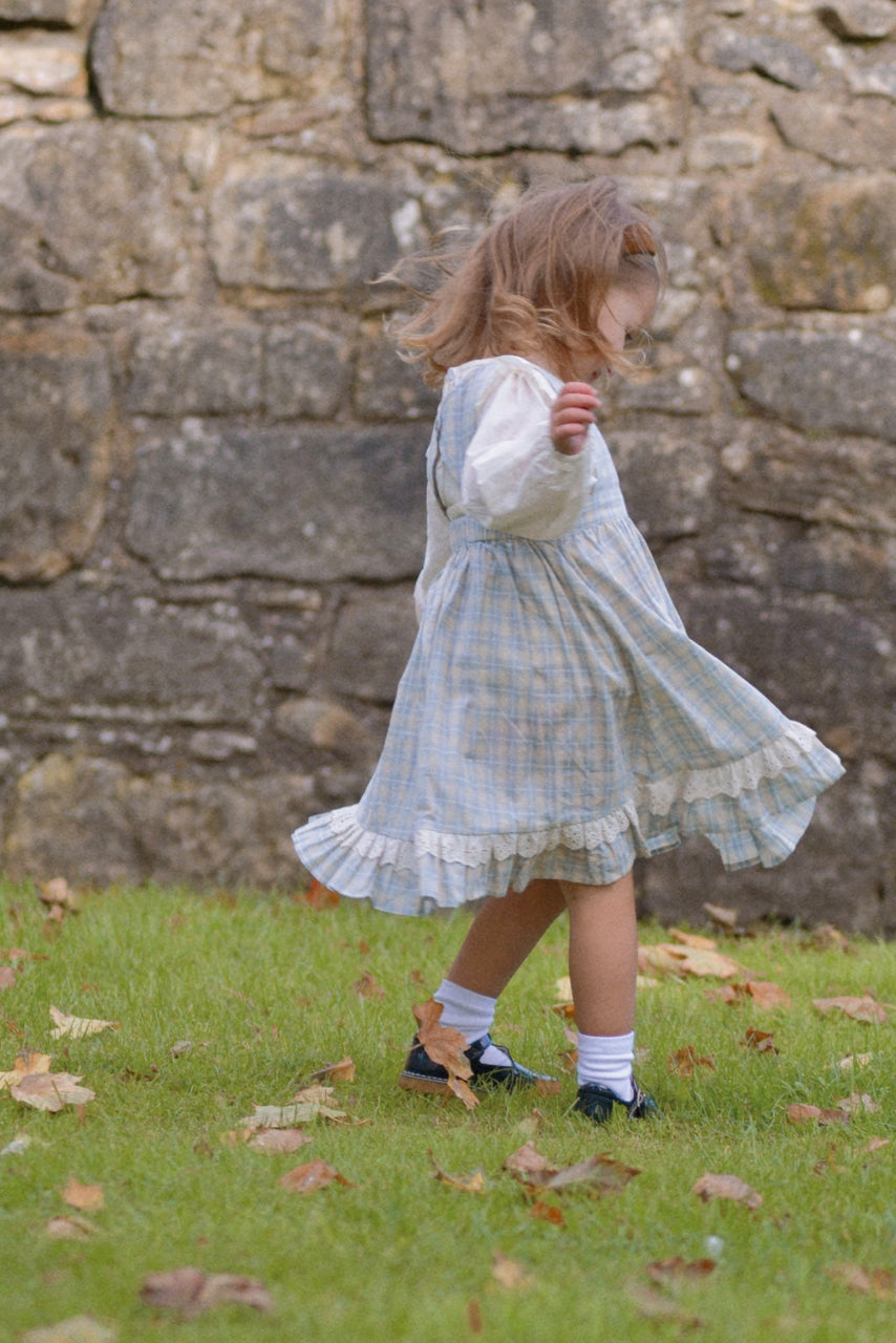 Child in a light blue dress standing in front of a stone wall