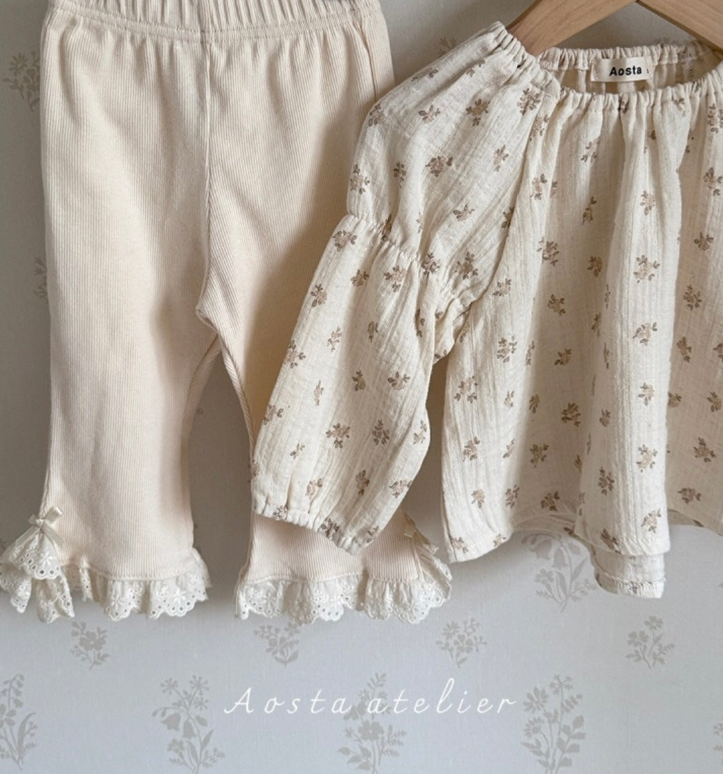 1 pair of baby pants, one plain and one children's blouse a floral pattern, on a hanger with a neutral background.