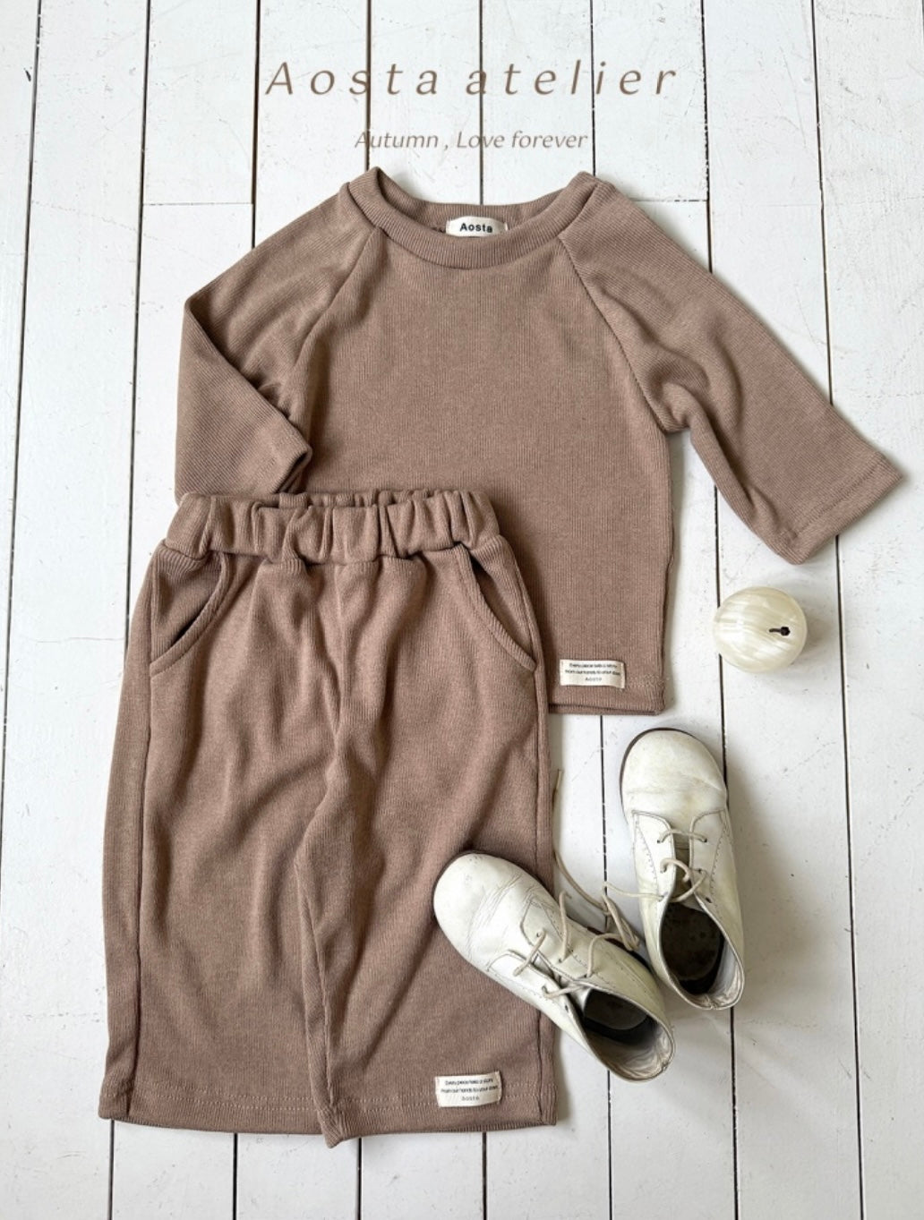 Brown long-sleeve dress with white sneakers on a light wooden floor, featuring 'Aosta atelier' branding.