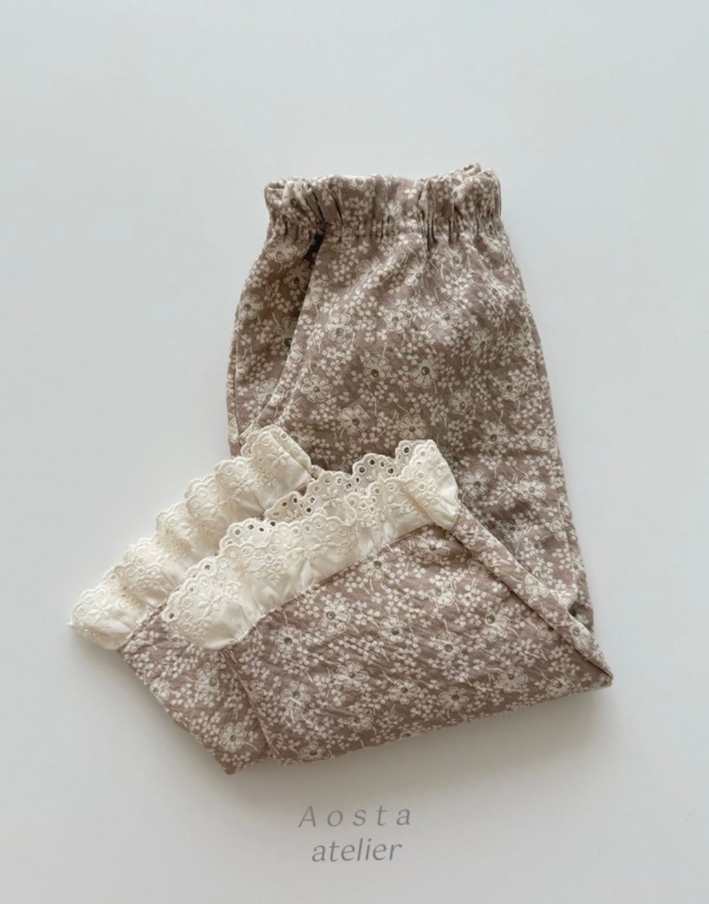 Floral-patterned fabric with lace trim on a light gray background, featuring the brand 'Aosta atelier'.