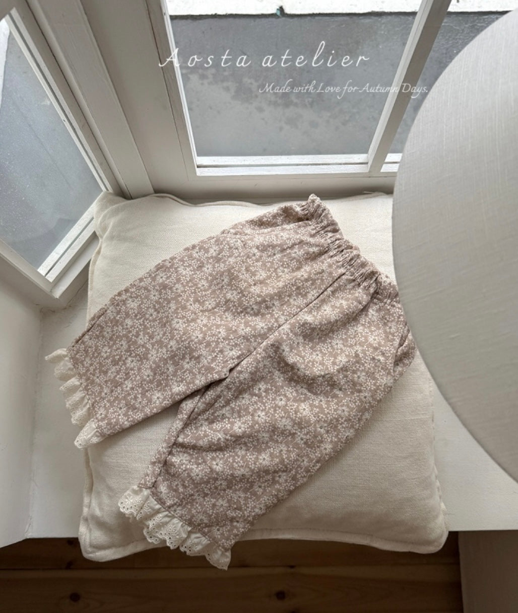 Floral-patterned blanket draped over a cushion on a wooden surface with a window in the background.