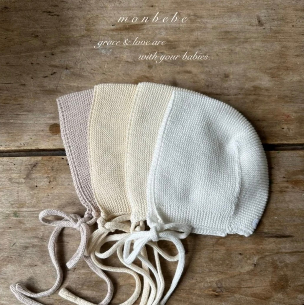 Knitted baby bonnet on a wooden surface with 'monbebe' branding.