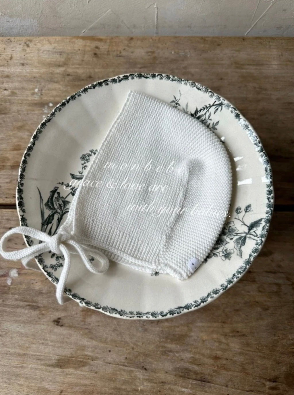 Knitted baby bonnet on a decorative plate with floral patterns