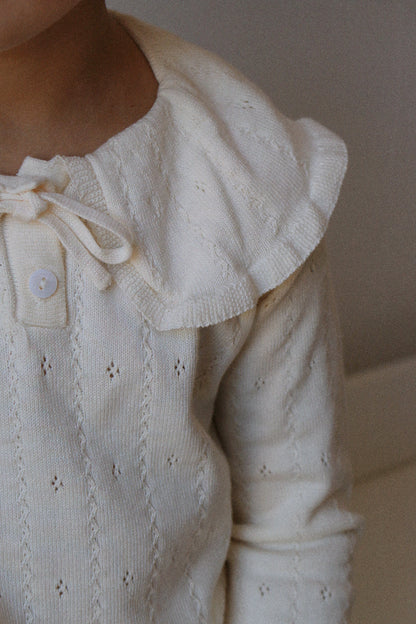 Close-up of a cream-colored knitted jumper with lace details on a plain background