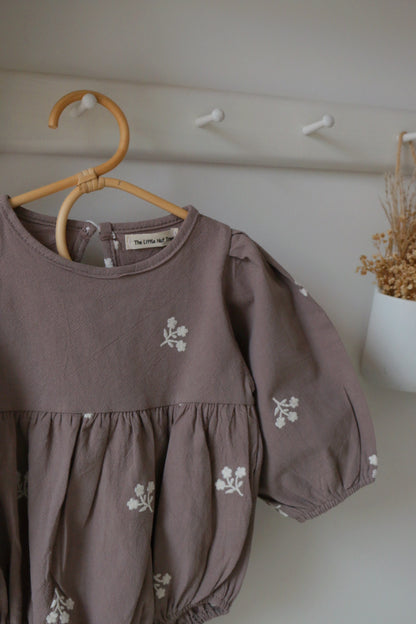 Grey Romper with floral embroidery on a wooden hanger against a neutral wall.