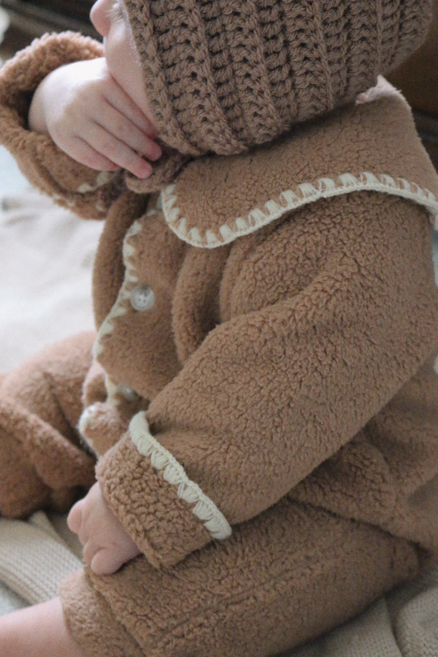 Close-up of a child wearing a brown fleece outfit with cream trim.