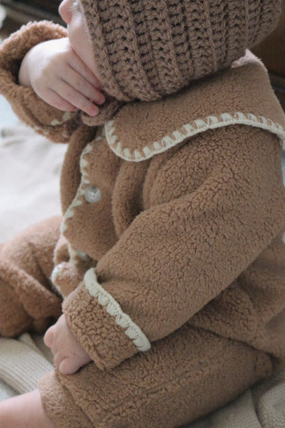 Close-up of a child wearing a brown fleece outfit with cream trim.