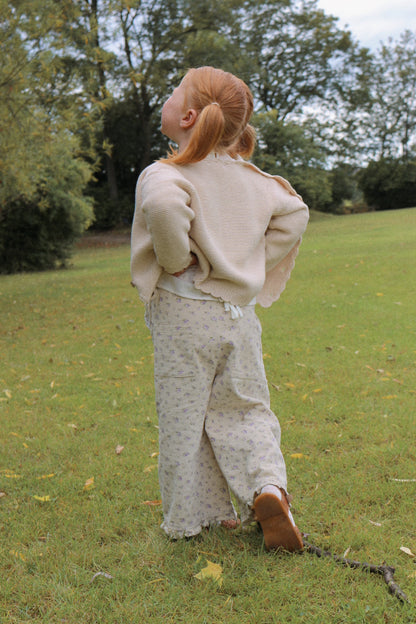 Girl wearing a beige outfit standing in a grassy field with trees in the background