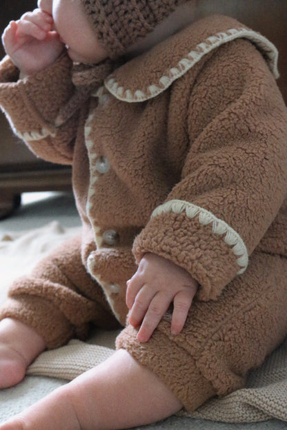 Close-up of a baby wearing a brown fleece outfit with white trim.