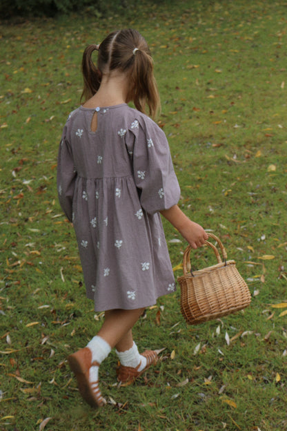 Child in a purple dress holding a wicker basket on a grassy field