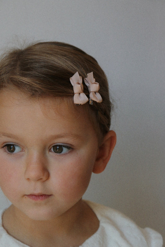 Young girl with two beige hair bows on a plain background