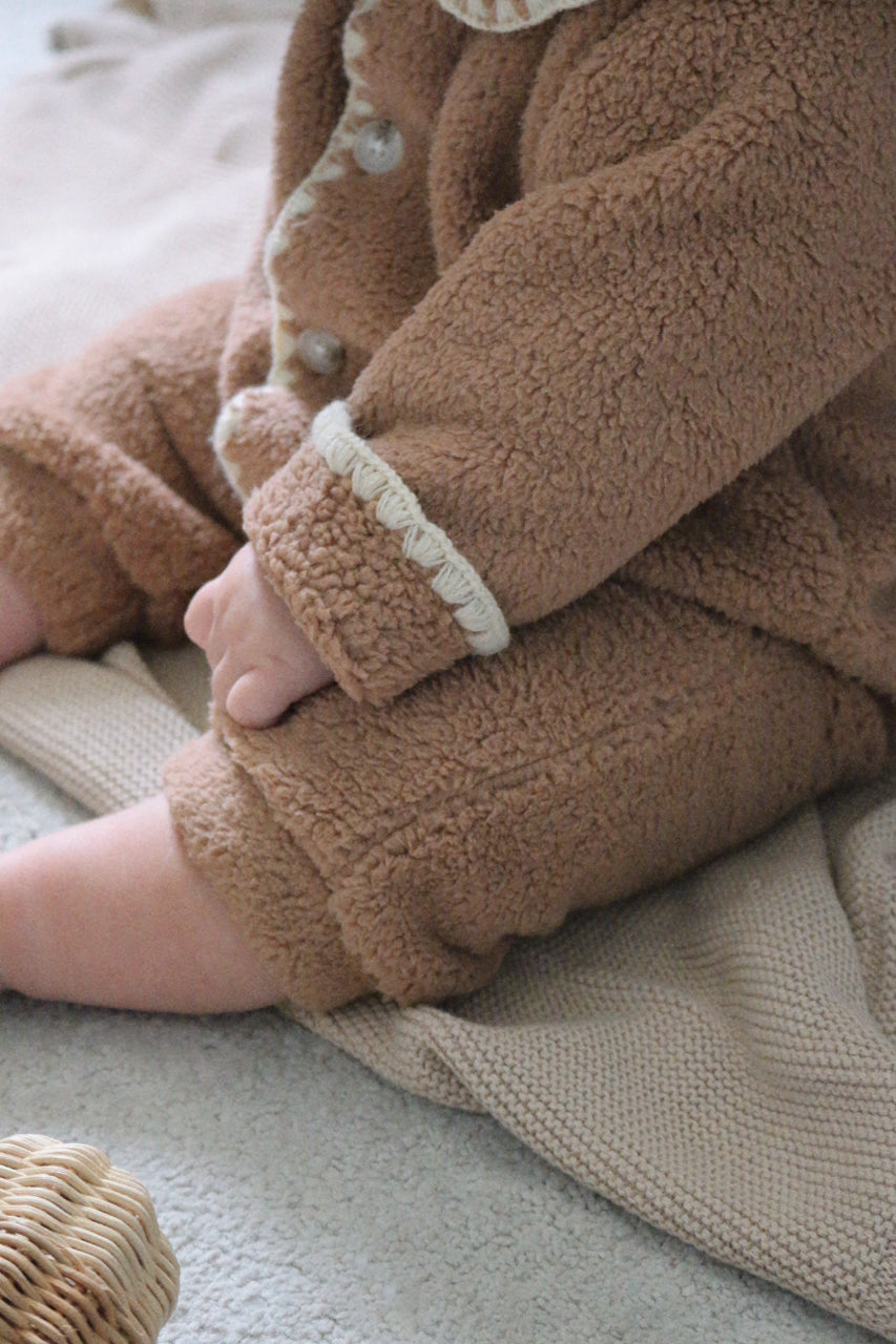 Close-up of a baby's legs in brown fleece pants on a neutral background