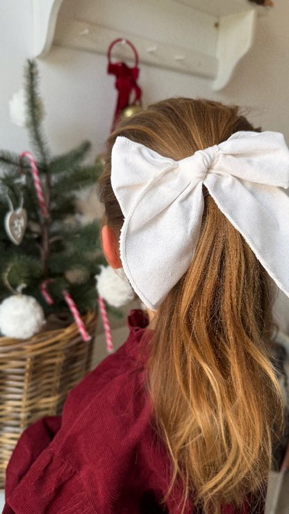Person with a large white bow in their hair, standing in front of a decorated Christmas tree.