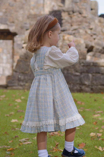 Young girl in a blue checkered dress standing in front of stone ruins.