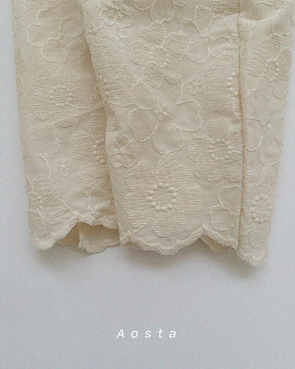 Close-up of beige lace pant cuffs with 'Aosta' branding on a light gray background
