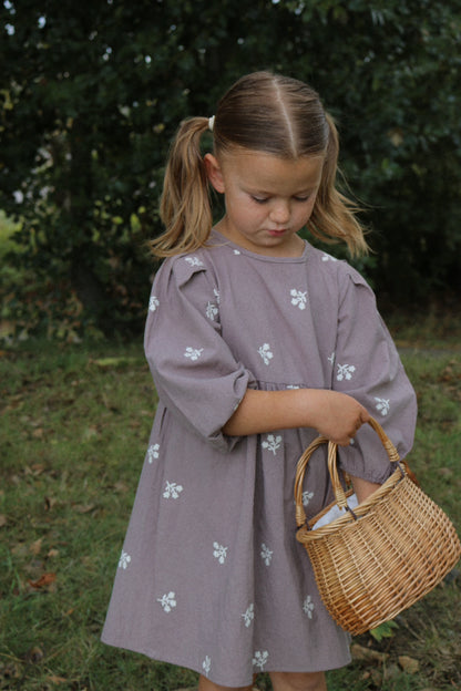 Young girl in a purple dress holding a wicker basket outdoors.
