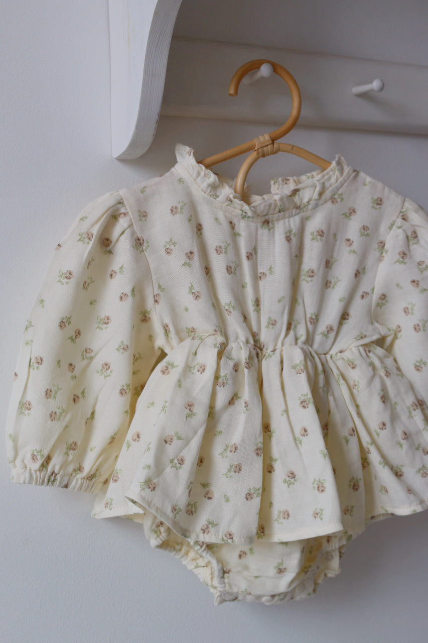 Baby skirted romper with floral pattern on a wooden hanger against a white wall