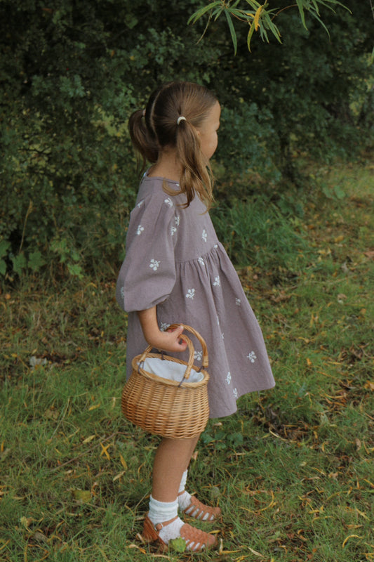 Young girl in a grey dress holding a wicker basket in a natural setting.