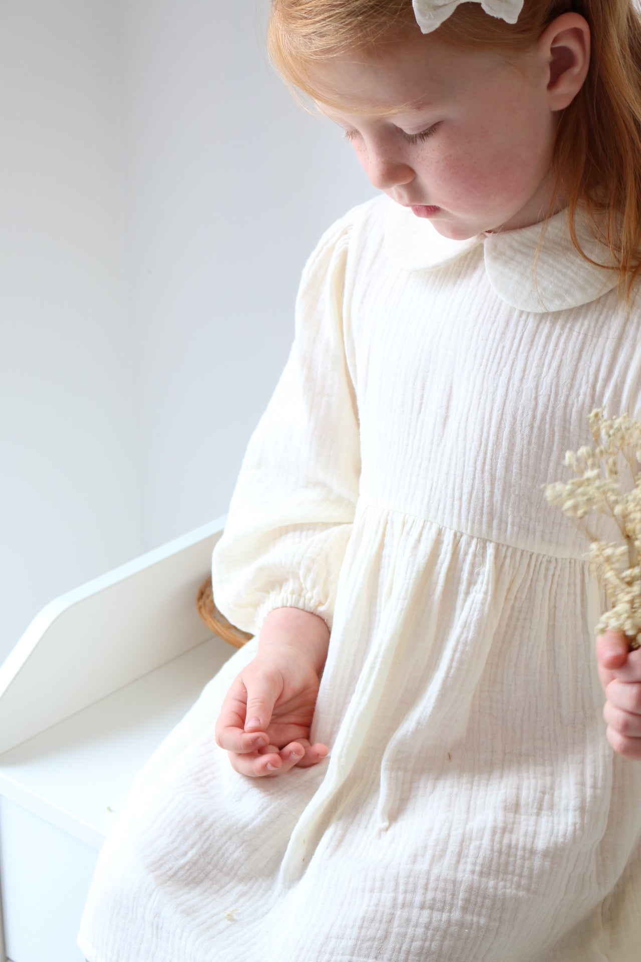 Girl n a cream dress holding dried flowers on a light background