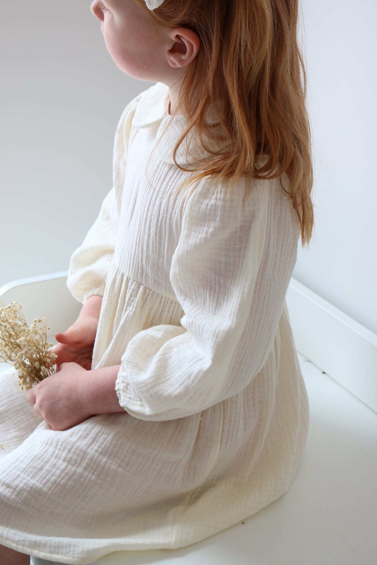 Child in a cream dress holding a gold flower on a white background