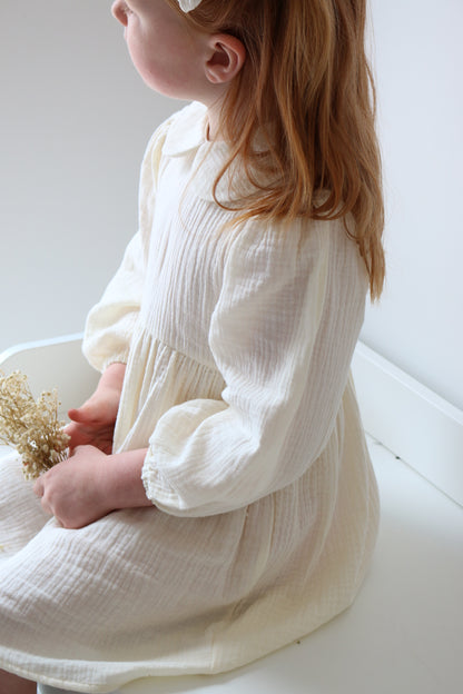 Child in a cream dress holding a gold flower on a white background