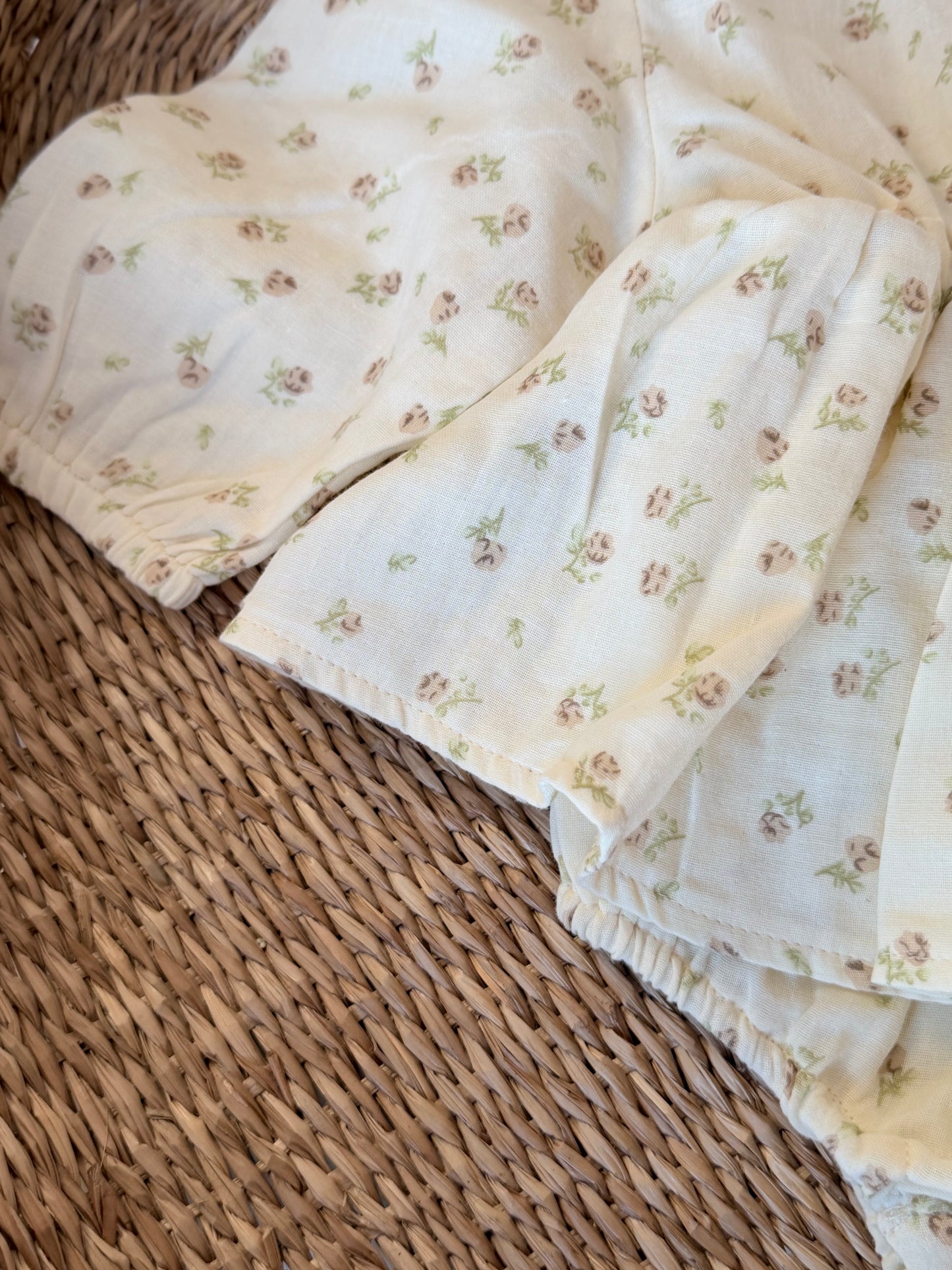 Close up of a cream Romper with floral print, flat laid on a wicker background.