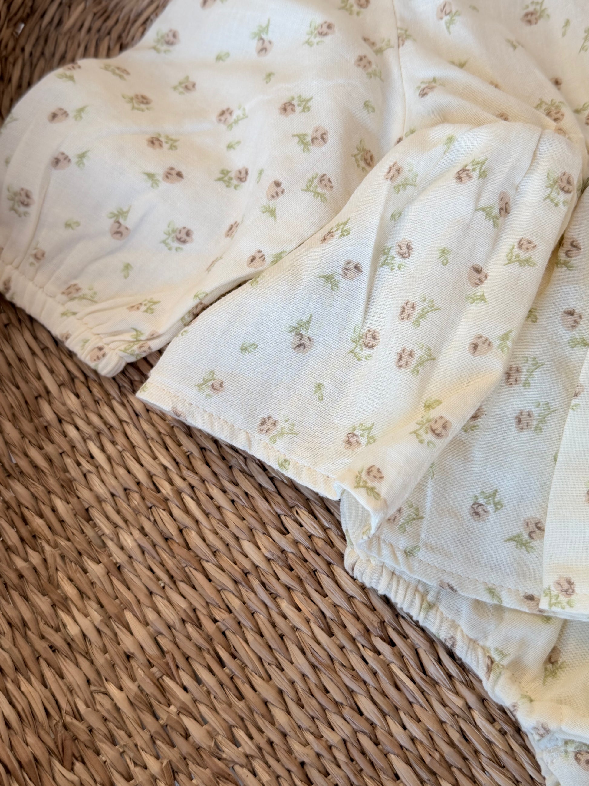 Close up of a cream Romper with floral print, flat laid on a wicker background.