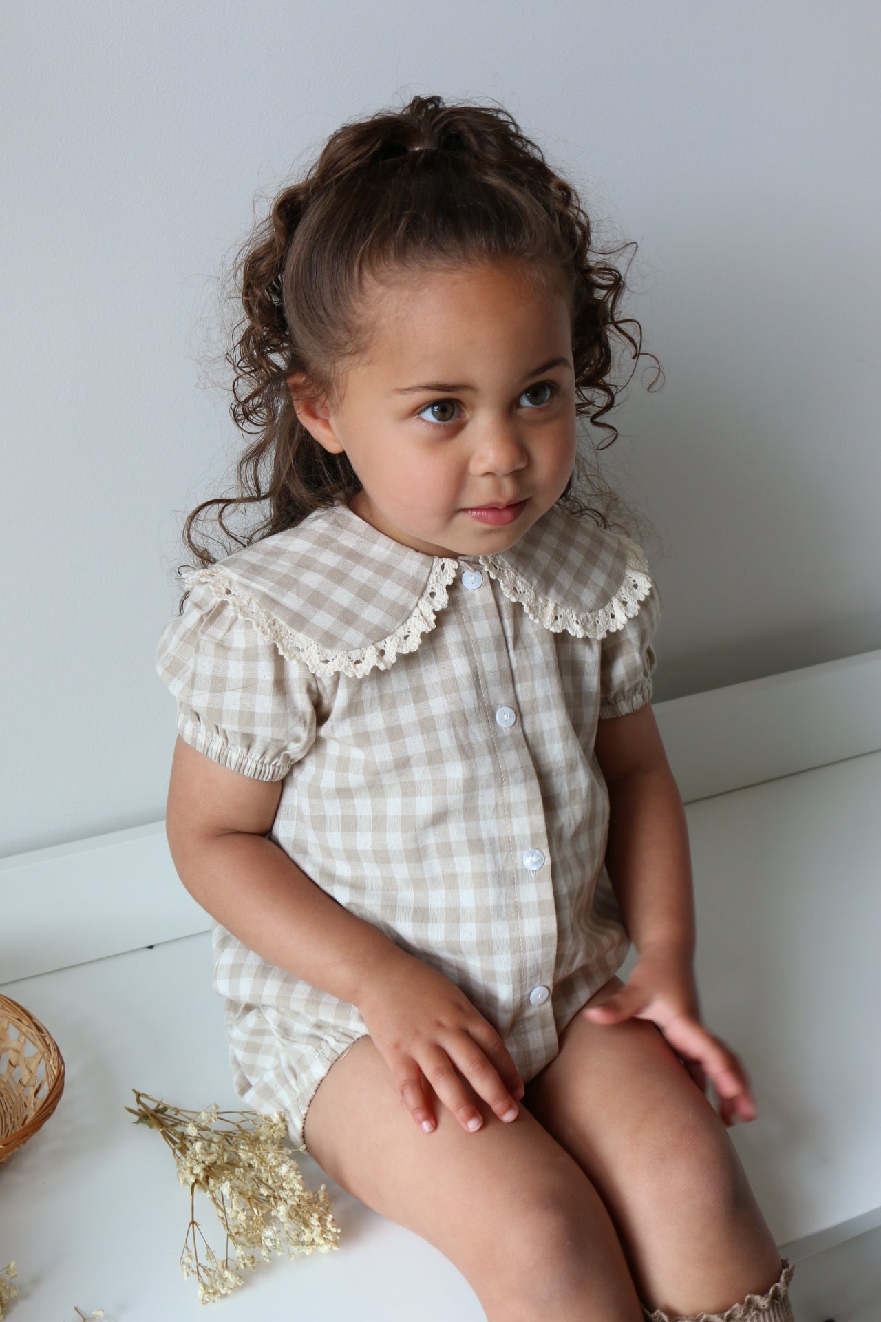 Young girl in a checkered romper sitting on a white drawers