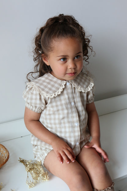 Young girl in a checkered romper sitting on a white drawers