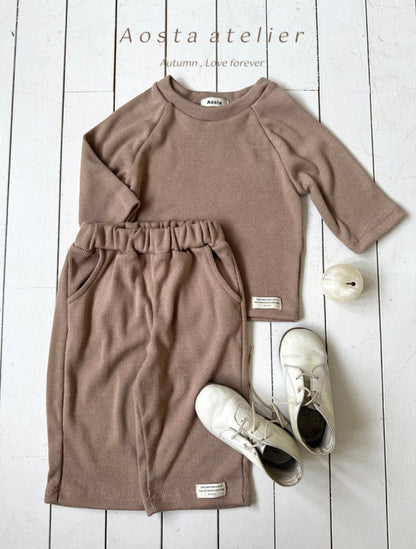 Brown long-sleeve dress with white sneakers on a light wooden floor, featuring 'Aosta atelier' branding.