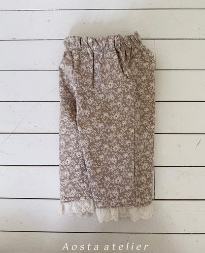 Floral patterned pants with lace trim on a white wooden background, branded 'Aosta atelier'.
